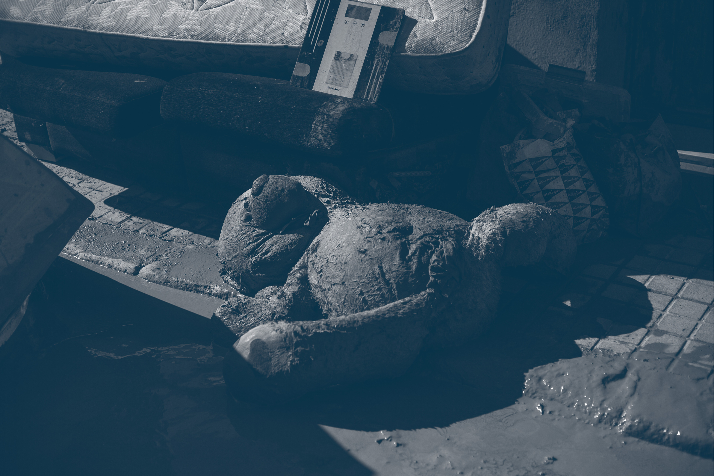Un peluche cubierto de barro junto a un colchón y mobiliario dañado